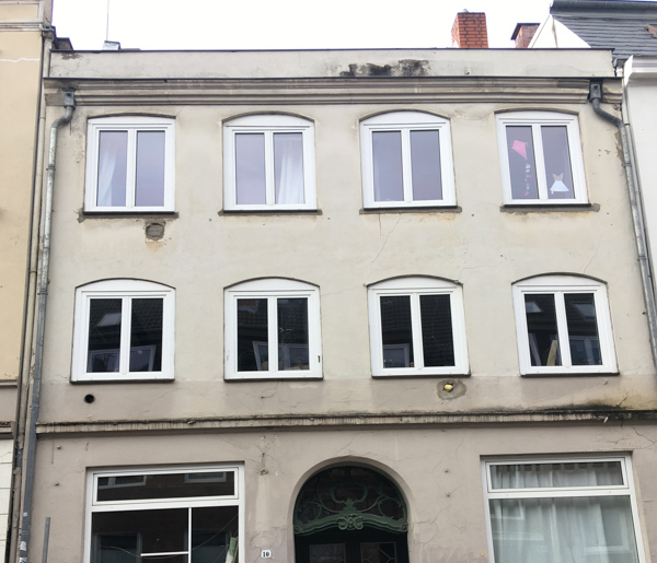 Das Haus vor der Sanierung mit grauer Fassade und ungeteilten weißen Fenstern